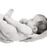 black and white image of a newborn baby cupped in both parents hands from the side