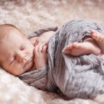 newborn baby curled on back swaddled in soft grey blanket