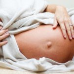 pregnant mum lying on her side, draped in fabric, showing her hand on bump