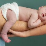 Sleeping newborn baby lying suppported on both parents arms