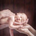 close up of sleeping newborn baby cupped in parents hands