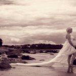 fine art pregnant woman from the side draped in fabric standing on the beach