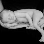 close up of sleeping newborn baby cupped in parents hands