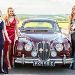 Three glamorous prom guests posing in front of their jaguar