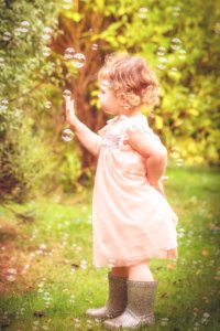 Toddler in pink dress and wellies studying bubbles