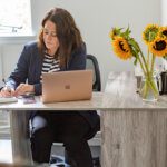 Business woman working at her desk with a vase of sunflowers and laptop