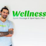 Tattooed masseuse standing next to his green business sign