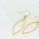 oval gold dangly earrings on a leaf skeleton and watercolour paper