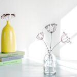 Sunlight streaming through a window highlighting wire flowers in a glass vase