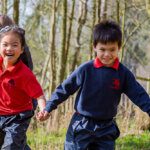 Three junior school students laughing, holding hands and running through a wood