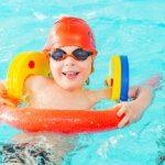 Boy in a colourful inflatable ring wearing goggles in a swimming pool