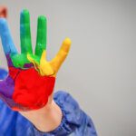 close up of boy holding up his hand with lots of colourful paint